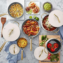 Cream ceramic pots and pans with gold handles, arranged around food-filled cookware