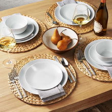 Round woven water hyacinth placemat in natural color, with folded gray napkin atop.