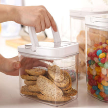 Hand opening a clear flip-lock pantry container, revealing cookies inside