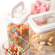 Clear flip-lock pantry containers with lids open, showing snacks and candy inside