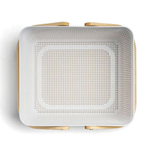 Square white storage basket with perforated sides and light wood side handles.
