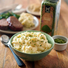 Bowl of mashed potatoes topped with chopped chives, with seasoning jar nearby