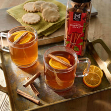 Cinnamon sticks jar with mugs of spiced drink and orange slices on tray
