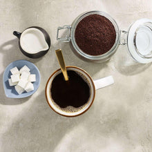 Brewed dark coffee in a cup with sugar cubes and open coffee container