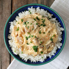 Bowl of long grain rice topped with creamy sauce and chopped herbs