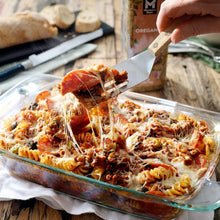 Hand sprinkling oregano over baked pasta in a glass dish