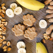 Paw-shaped dog treats with banana slices and peanuts on a wooden surface