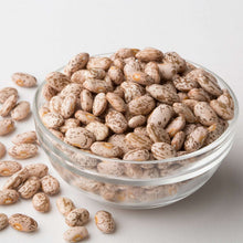 Glass bowl of pinto beans with scattered beans around