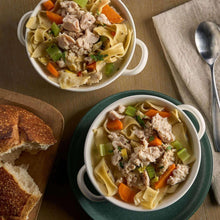 Two bowls of chunk chicken pasta with carrots, peas, and spinach, plus bread