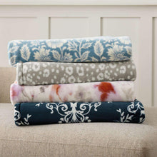 Stacked folded lounge throw blankets in blue floral, gray dot, and pink patterns