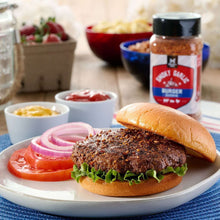 Smoky garlic burger seasoning shaker with burger and bun on plate, plus tomato and onion.