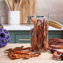 Jar filled with dried sweet potato fries dog treats and scattered pieces on countertop
