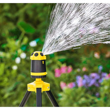 Telescoping tripod sprinkler close-up with yellow top and dark body, water spray streaming