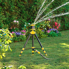 Telescoping tripod sprinkler spraying a fan of water above flowering garden beds