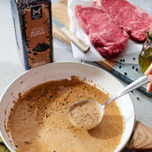 Creamy peppercorn sauce in a pan with spoon and pepper specks