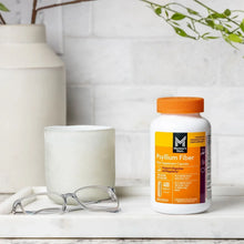 Psyllium fiber supplement capsules bottle with orange cap on tabletop beside glasses