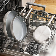 Stainless steel cookware set placed in dishwasher rack with lids and handles