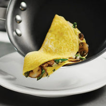 Nonstick fry pan holding a folded omelet with vegetables and toppings
