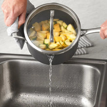 Nonstick saucepot with chopped vegetables as water pours in, dark gray aluminum
