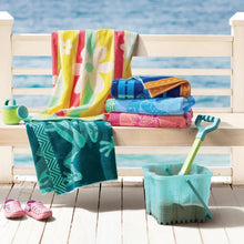 Kids beach towels stack on a bench: yellow, green, blue, and pink floral designs