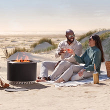Smokeless wood fire pit on sand with flames and round mesh base