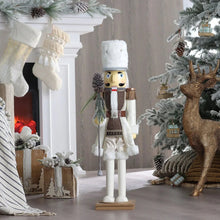 Standing wooden nutcracker figure with white tall hat, red sash, brown vest, holding brush.
