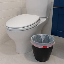 Small trash bag liner in a black bin with pink rim next to a white toilet
