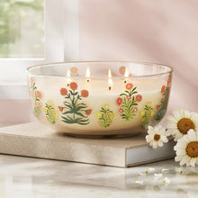 Floral glass candle jar with orange and coral flowers print and lit wicks, white wax