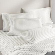 White sheet set with thin gray stripe print, neatly layered on a bed with pillows