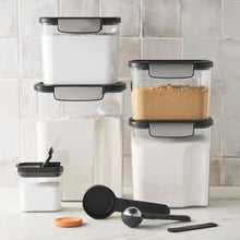 Set of clear Tritan food storage containers with black lids and measuring utensils