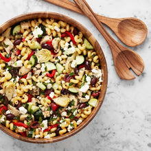 Acacia salad bowl with wooden servers, filled with pasta salad and chopped vegetables