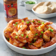 Bowl of saucy shrimp topped with green onions with Bang Bang seasoning bottle nearby