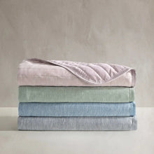 Cooling throw blanket stack in pink, sage, gray, and blue tones, quilted with stitched channels