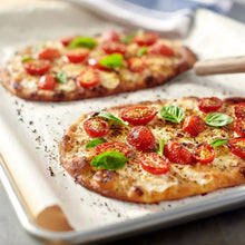 Flatbread pizza topped with basil leaves and tomato pieces on parchment