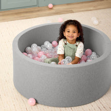 Gray foam ball pit with pink, white, and clear balls, kid seated inside