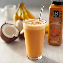 Turmeric-colored smoothie in a clear glass with a spoon, plus spice jar nearby