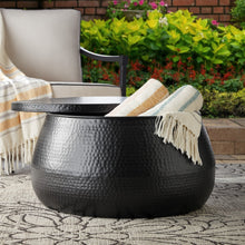 Round black hammered metal coffee table with storage, lid open showing throw blanket