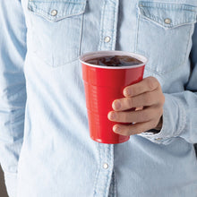 Red disposable plastic party cup held in a hand, filled with ice