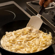Silicone scraper lifting creamy noodles from a black skillet
