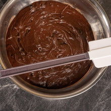 Silicone scraper spreading dark chocolate paste across a metal mixing bowl