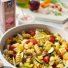 Pasta salad in a bowl with vegetables and pink salt granules.
