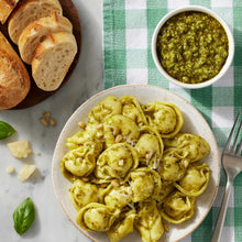 Basil pesto pasta in a bowl with grated cheese, basil leaves, and bread slices.