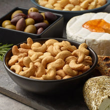 Bowls of lightly salted whole cashews with cashew pieces in foreground