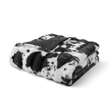 Folded faux fur throw blanket with black-and-white cow print design.