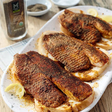 Black pepper-seasoned tilapia fillets on a baking tray with lemon wedges