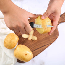 Paring knife peeling a potato on a wooden cutting board; black textured handle