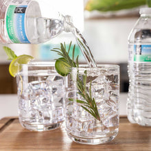 Purified water bottle pouring into clear glass with ice and rosemary