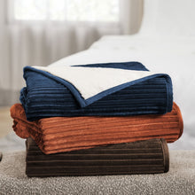 Stack of ribbed throw blankets: dark blue, rust brown, and dark brown