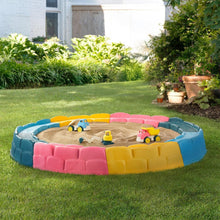 Children's inflatable sandbox with colorful padded border and toy trucks in sand.