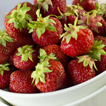 Red strawberries in a white bowl with green leaves
